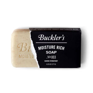 The cream-colored bar of Buckler's Moisture Rich Soap bar is sliding out of a black sleeve that has been torn.