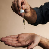 Man's hands squeezing Conditioning Beard Absolute white dropper with gold liquid onto palm of hand