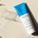 Skin Renewing Face Scrub white and blue tube on cream-colored table with glass of water
