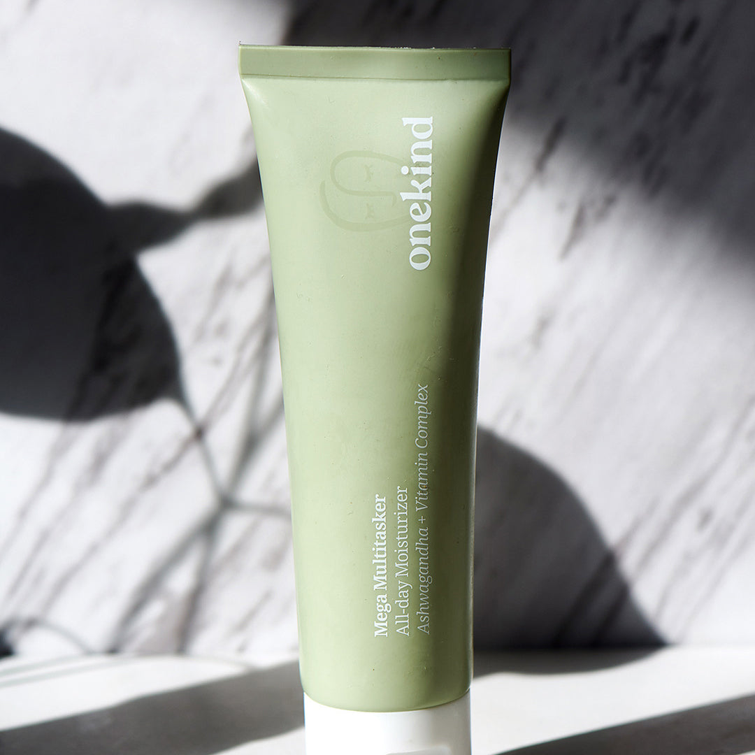 The Mega Multitasker All-Day Moisturizer in a sage green tube with a white cap stands against a marble gray and white background with shadows for contrast.