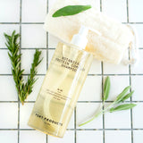 Port Products Botanical Protein Complex Shampoo bottle with gold liquid on white tile surface with rosemary and sage sprigs and loofah